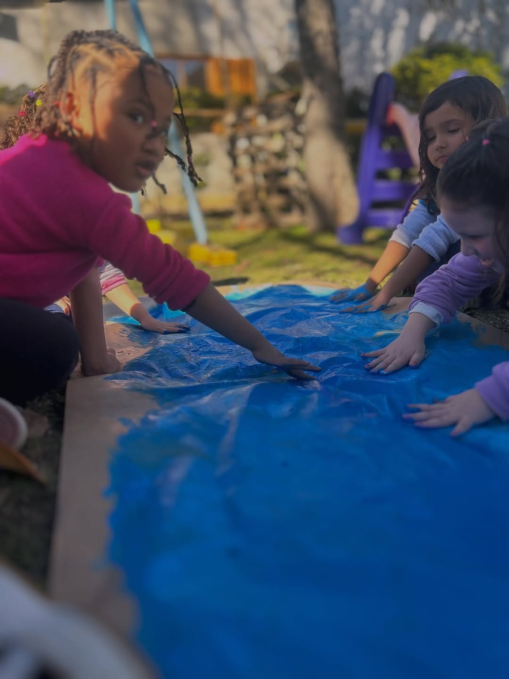 Crianças pintando juntas ao ar livre na Escola Amor de Mãe